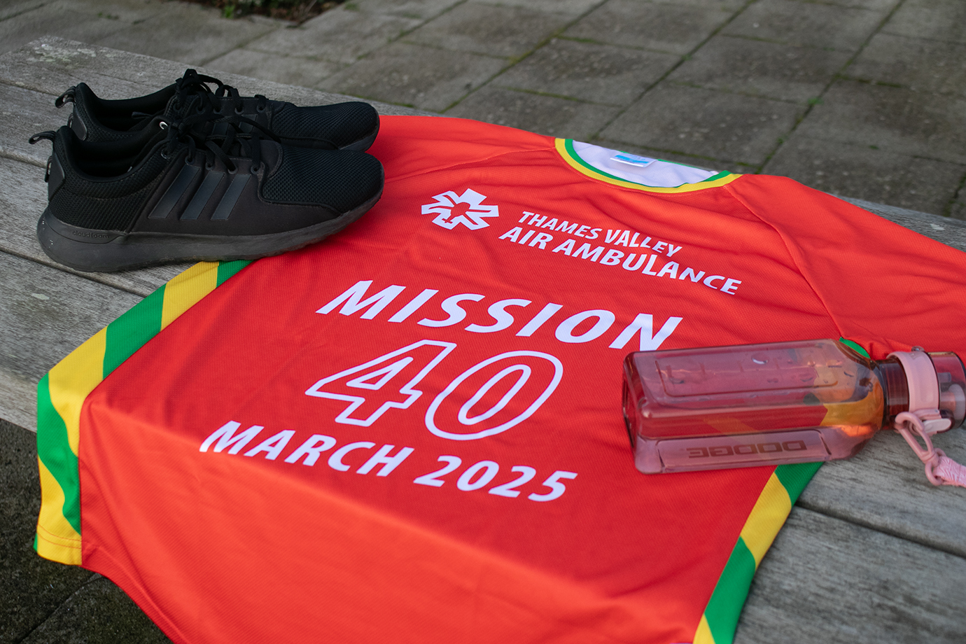 A red Mission 40 t-shirt laid on a bench next to a pair of trainers and a water bottle